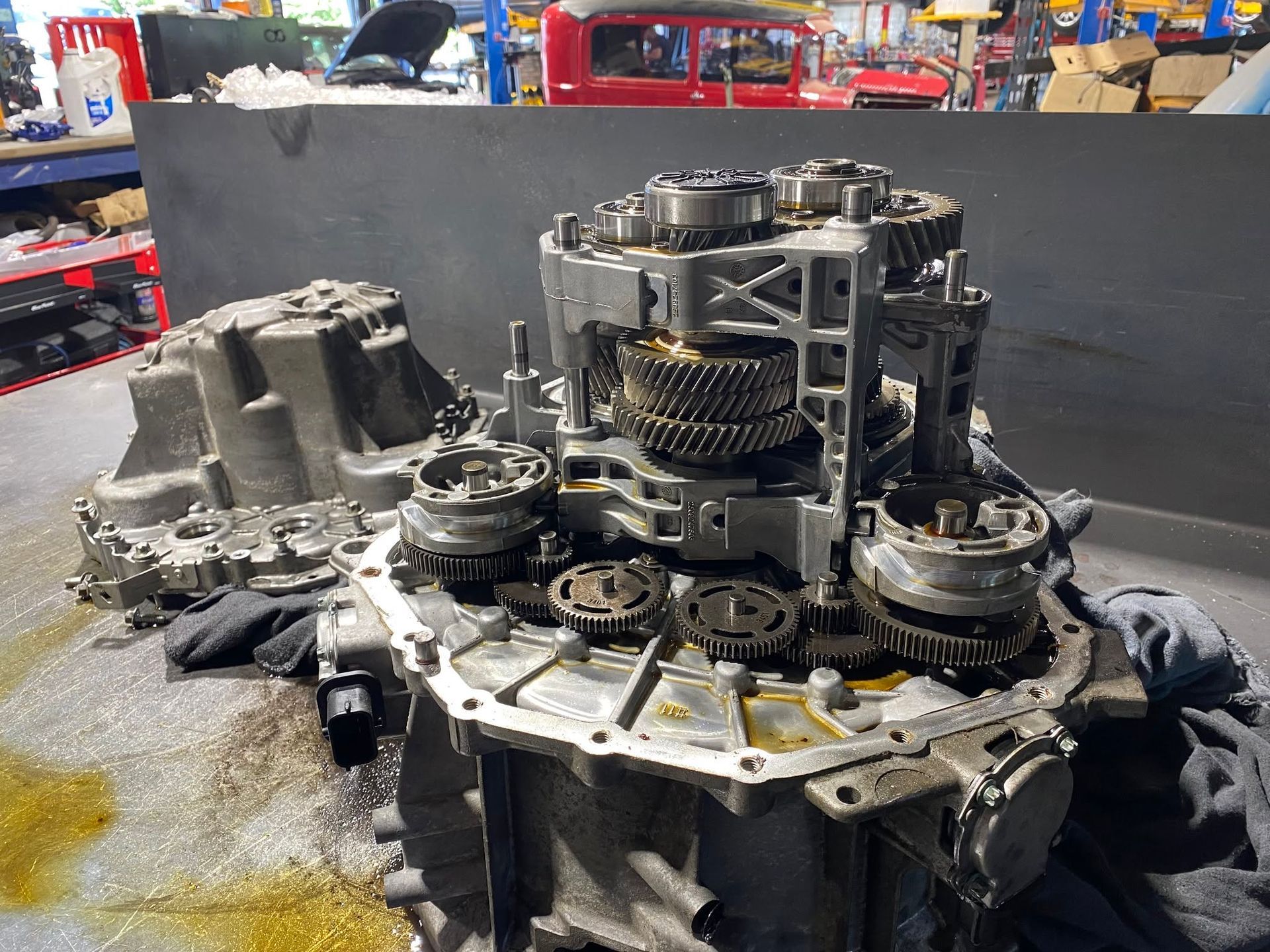 Disassembled automatic transmission on a workbench in a repair shop, with gears and metal parts exposed.