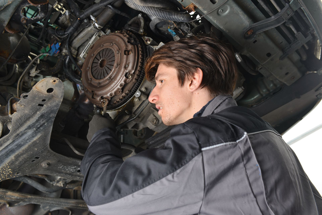 Man inspecting a car engine bay, with exposed mechanical parts under the hood