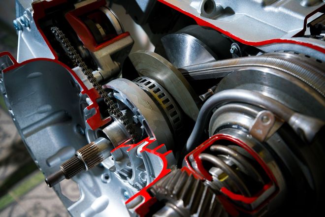 Close-up of a car engine with exposed belts, pulleys, and metal components in red and silver.