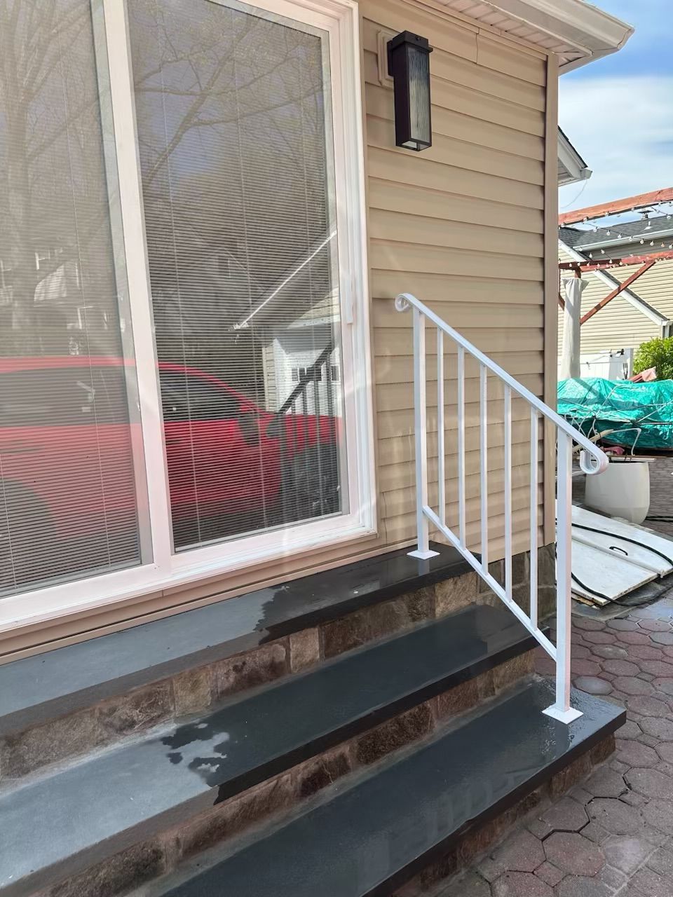 Front steps to a beige house with black treads and a white exterior stair safety railing for mobility access
