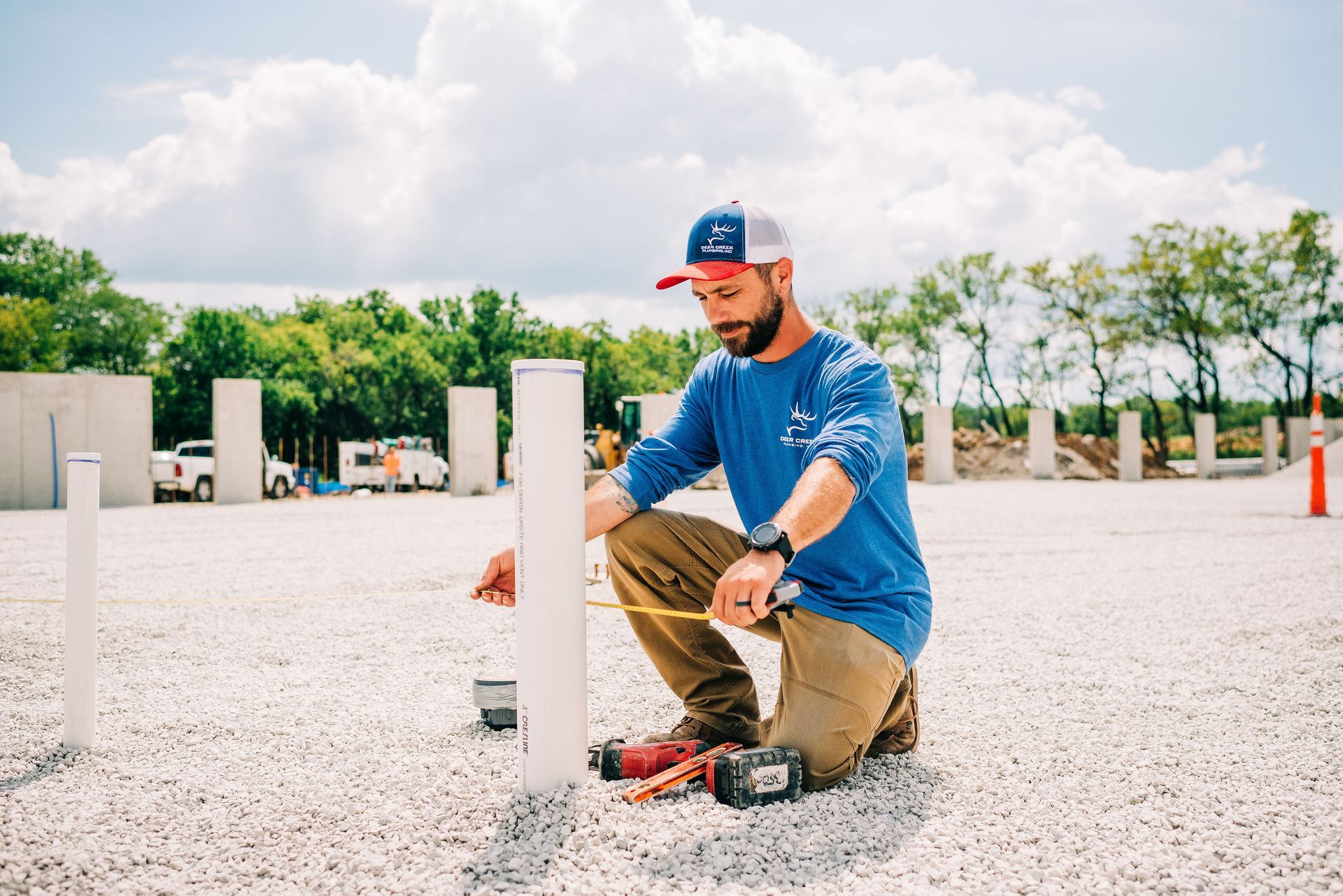 A man is kneeling down measuring a pipe with a tape measure.