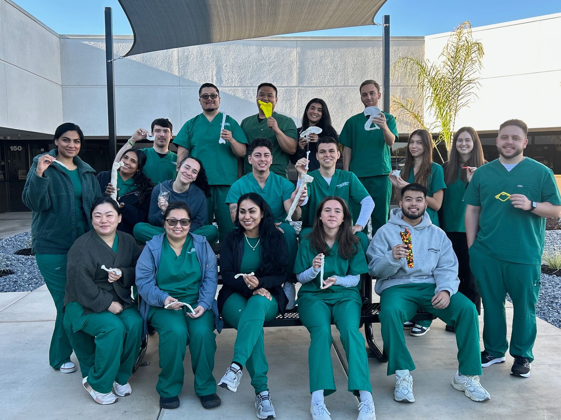 Group of people in green scrubs hold medical tools outdoors, smiling.