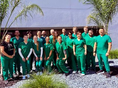 Group of people in green uniforms posing outdoors in front of a building