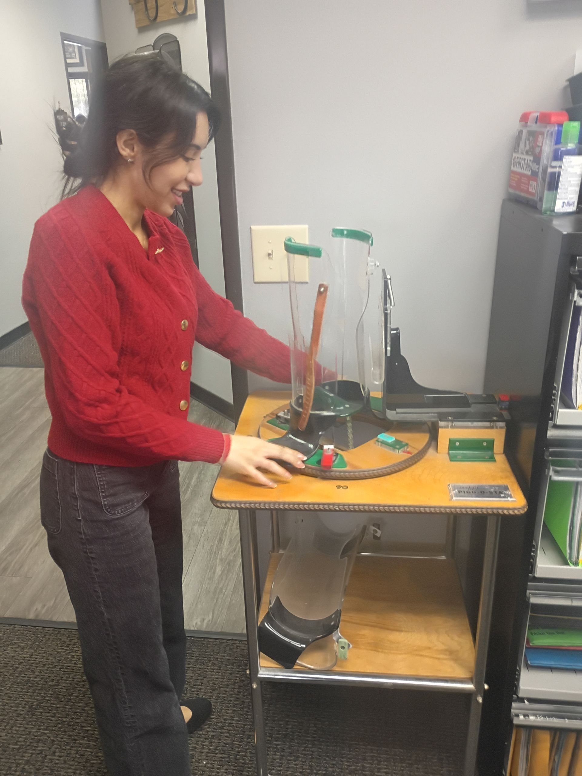 Woman in red sweater operating a science experiment with a tall glass cylinder on a wooden table.