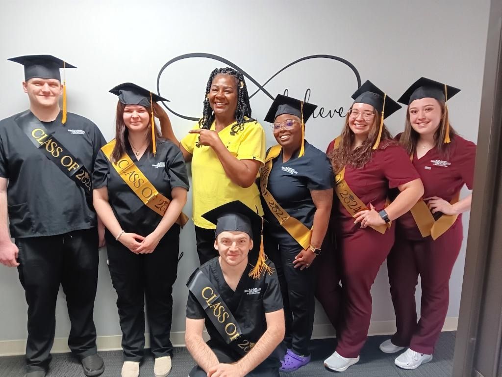 Group of graduates in caps and gowns, wearing sashes.  Wall with an infinity symbol.