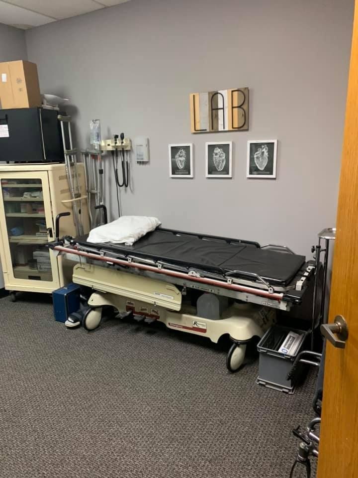 Medical exam room with a stretcher, lab equipment, and gray walls.