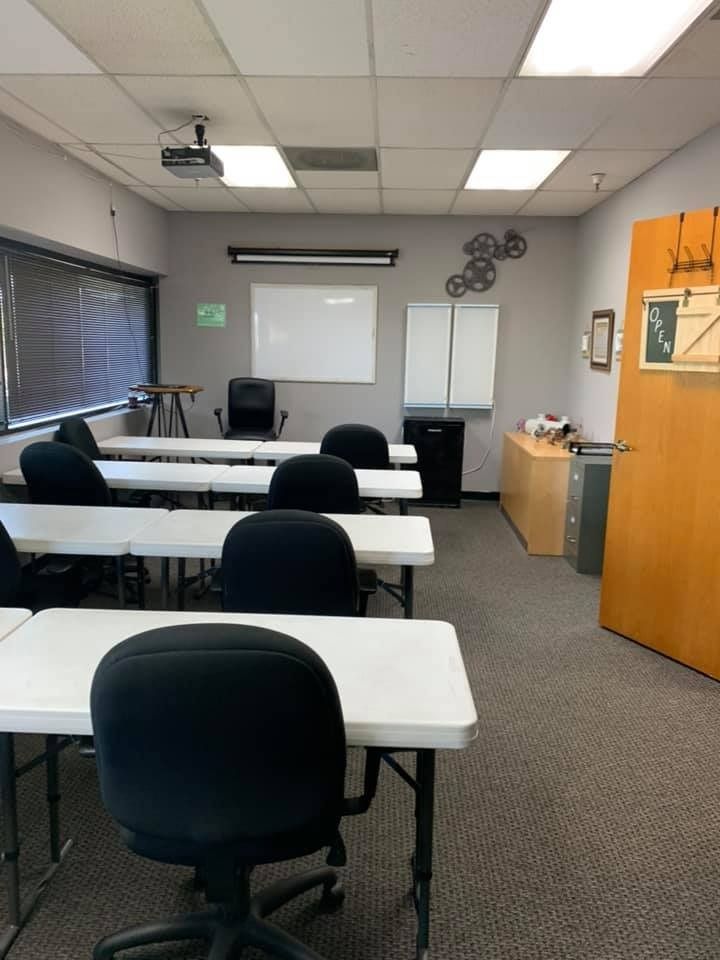 Classroom with white tables and black chairs, whiteboard, and window.