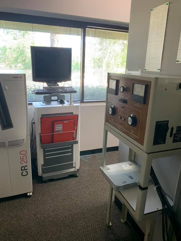 A medical office corner with a CR 25.0 machine, computer, and control panel stand near a window.