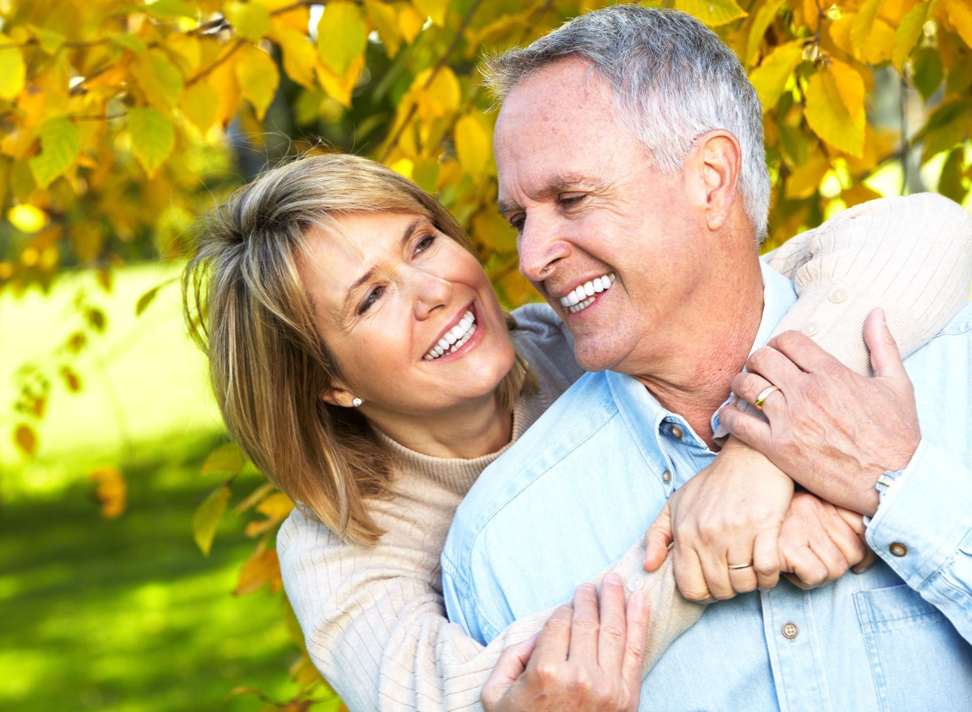 Smiling couple embracing outdoors with yellow leaves.