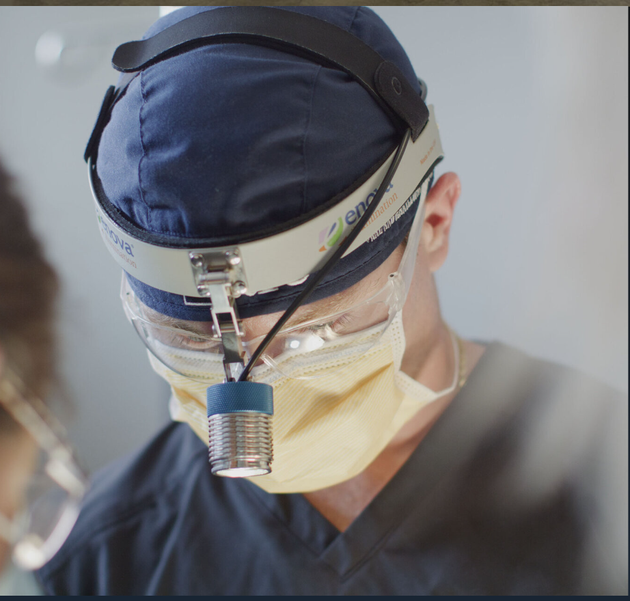 Surgeon wearing a surgical cap, loupes, and mask, focused during a procedure.