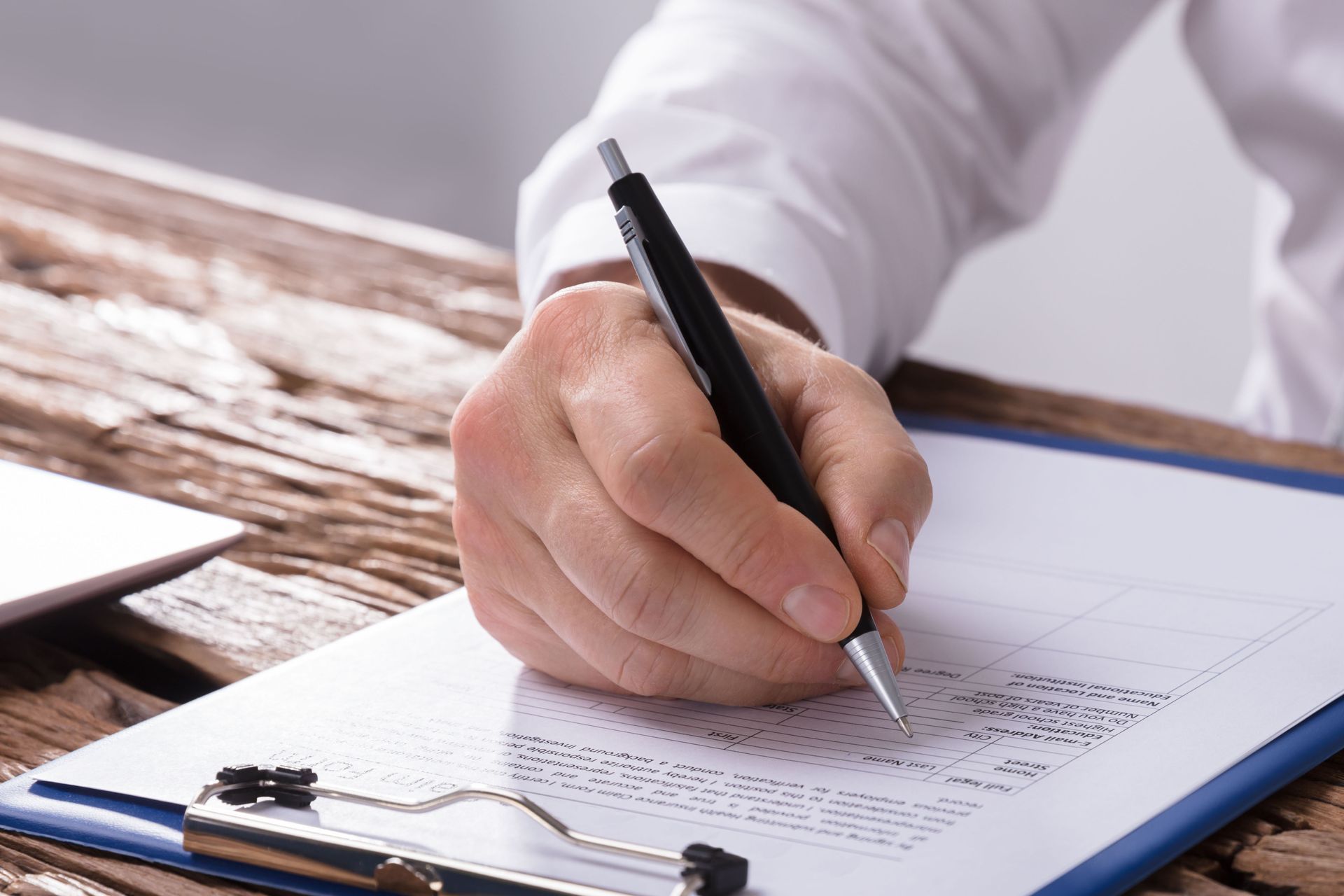 Hand writing on a clipboard with a pen on a wooden desk.