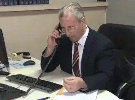 Two people stand in front of framed certificates. Woman in a dress, man in a suit.