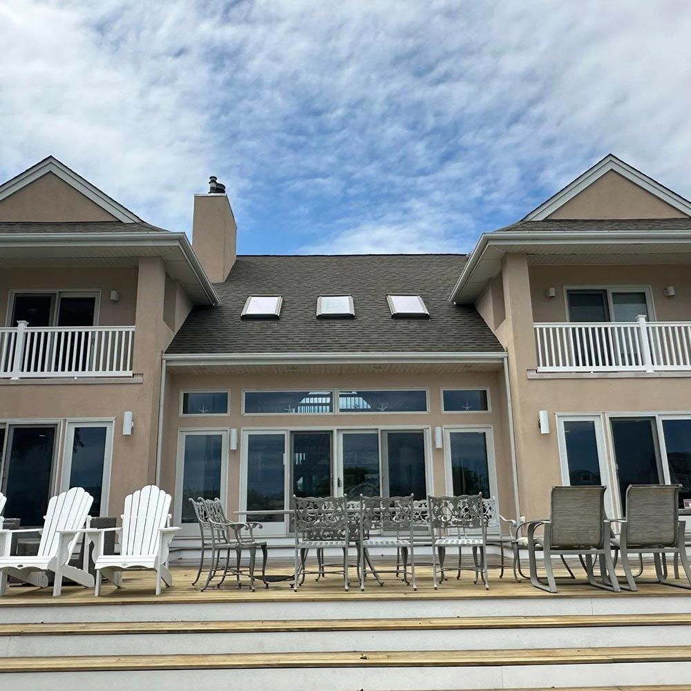 The back of a large house with tables and chairs on the deck