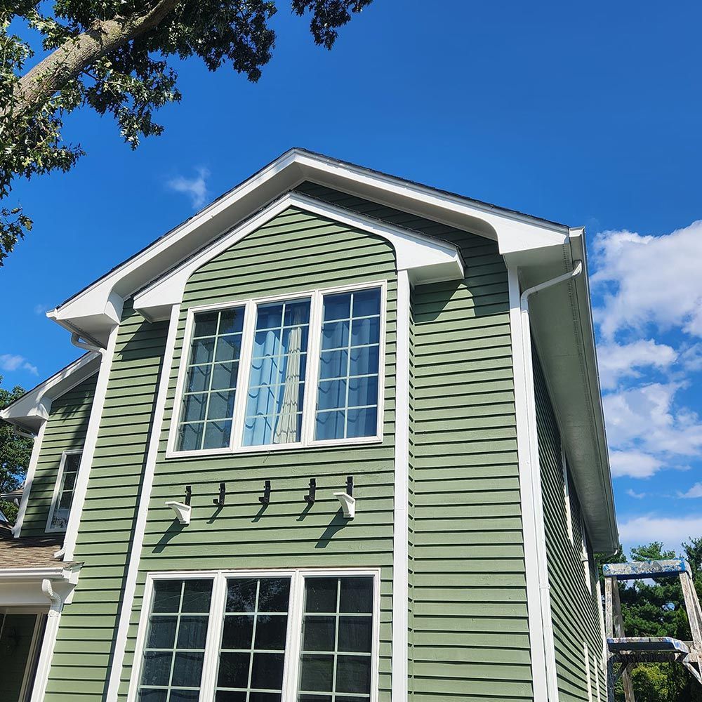 A green house with white trim and a blue sky in the background