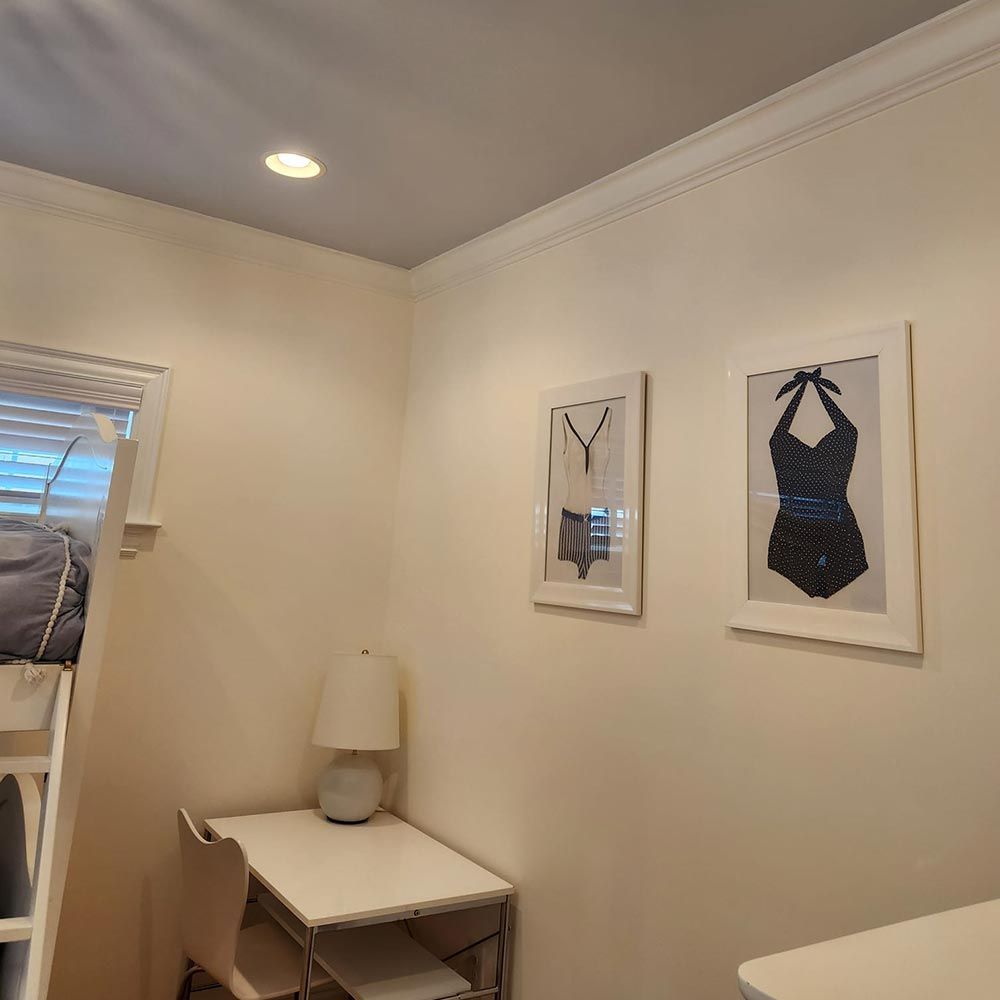A bedroom with a bunk bed , desk , chair , lamp and two pictures on the wall.