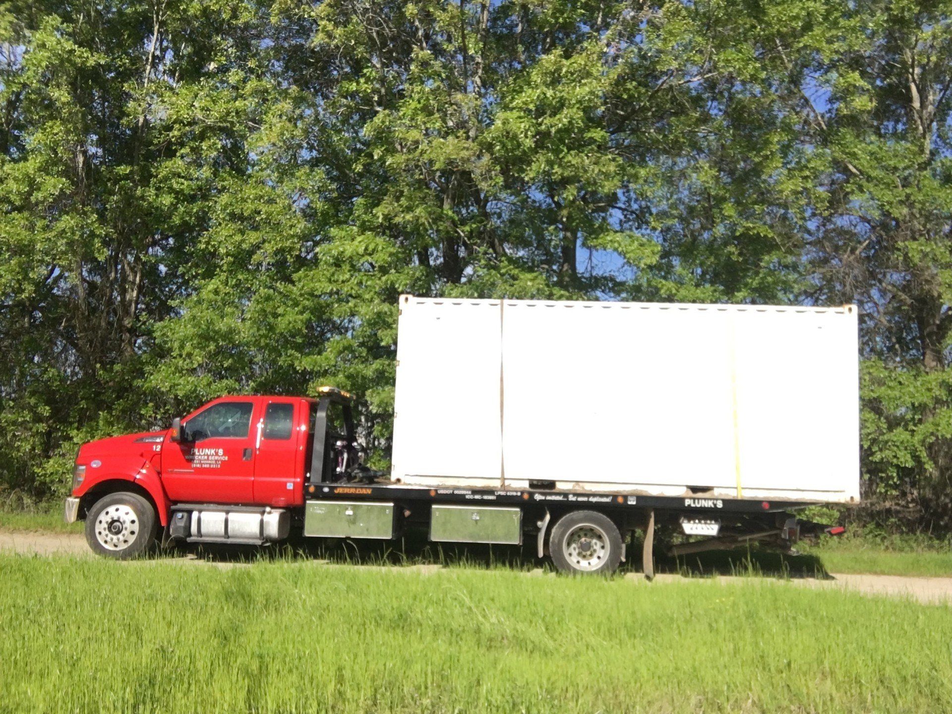 A red truck with a white box on the back is parked in a grassy field.