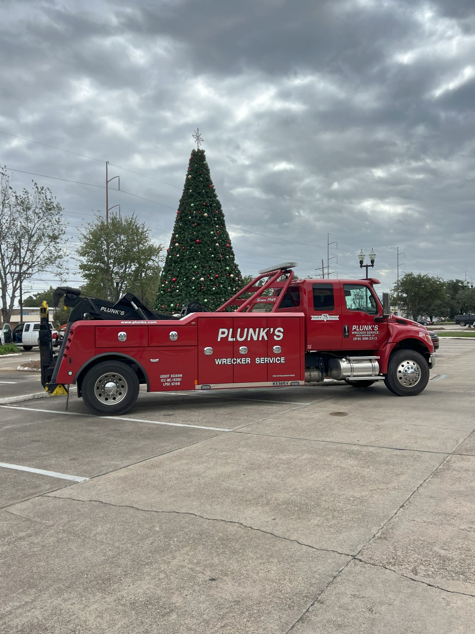 A red tow truck is parked in a parking lot next to a christmas tree.