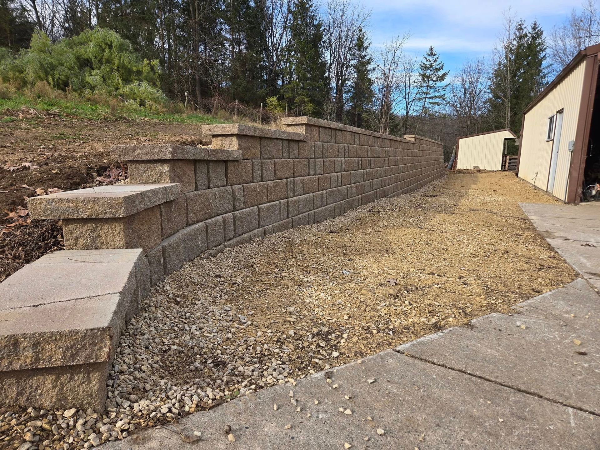 A brick wall is surrounded by gravel next to a sidewalk.