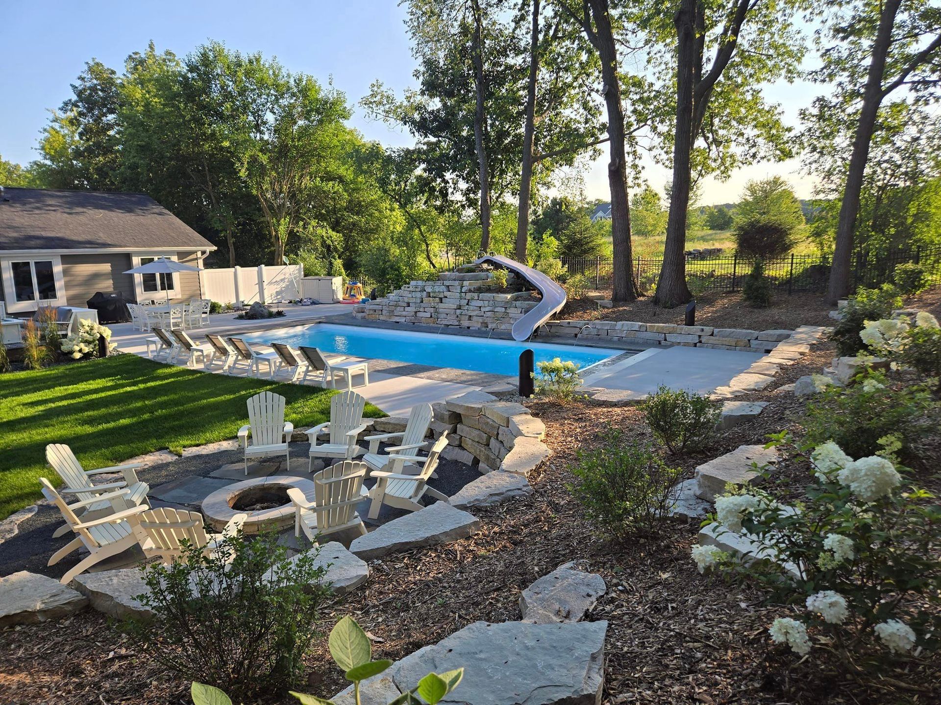 A large swimming pool is surrounded by lawn chairs and a fire pit.