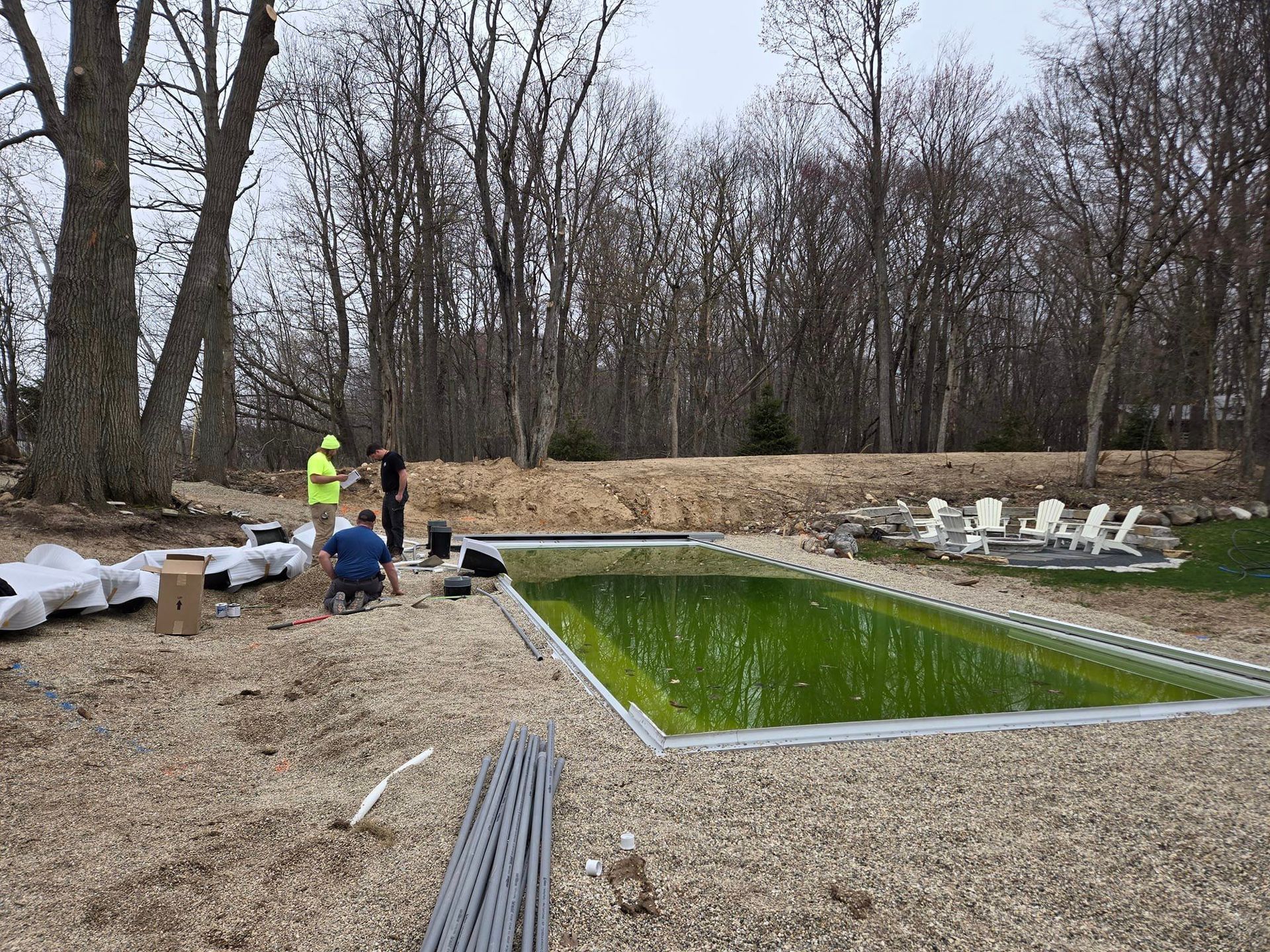 A group of people are standing around a large swimming pool surrounded by trees.