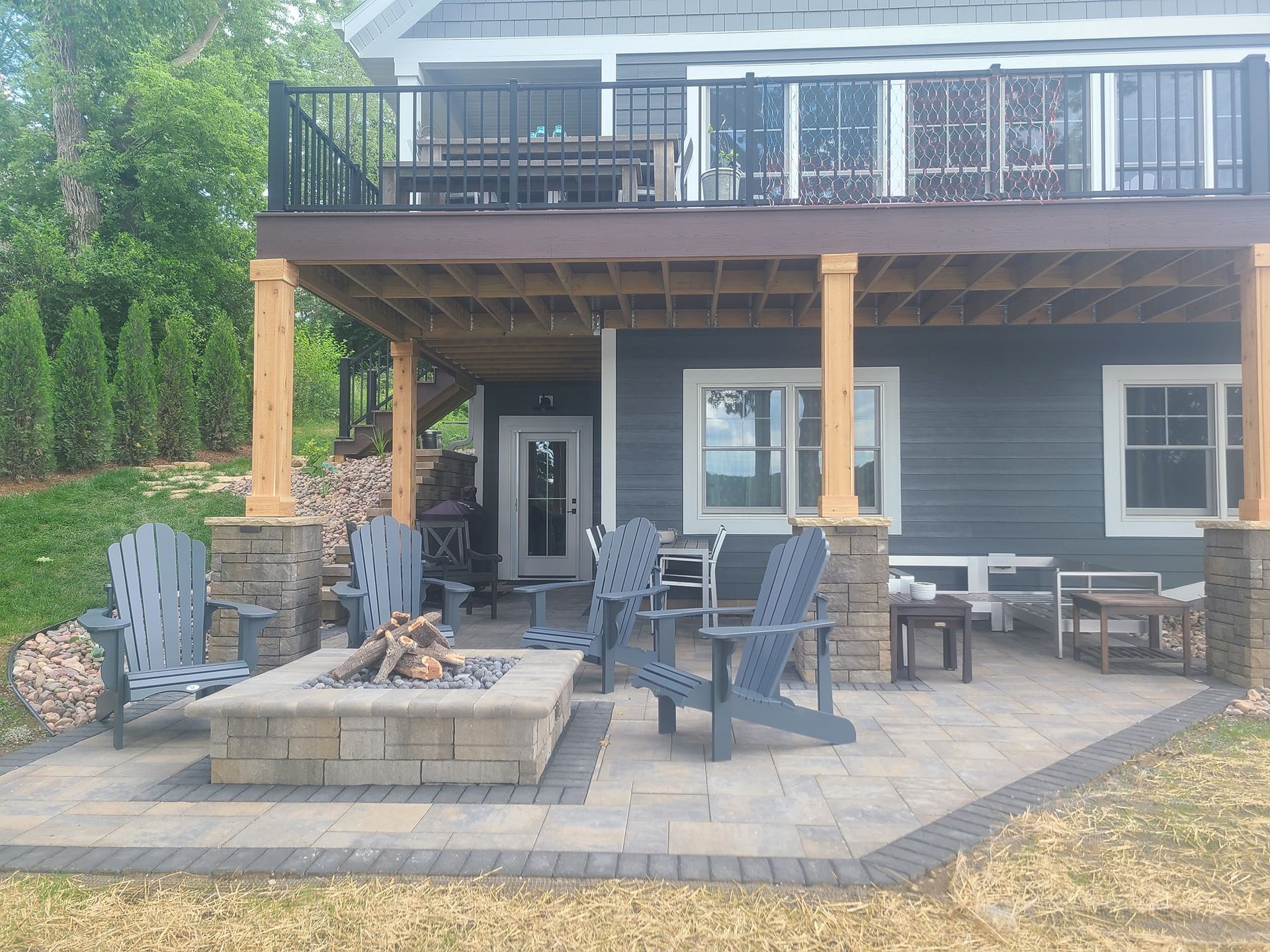 A patio with a fire pit and chairs in front of a house.