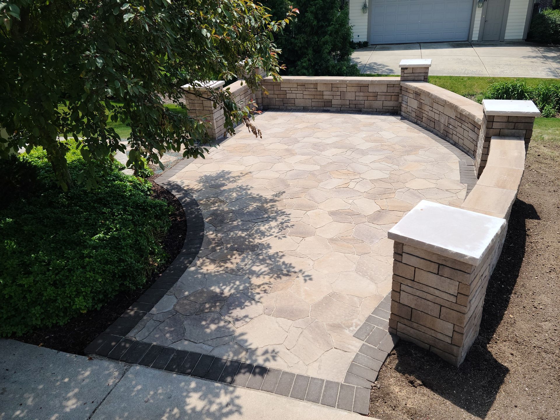 A patio with a stone wall and a bench in front of a garage.