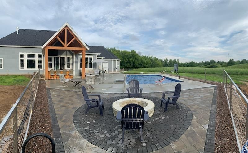 A fire pit is in the middle of a patio next to a pool.
