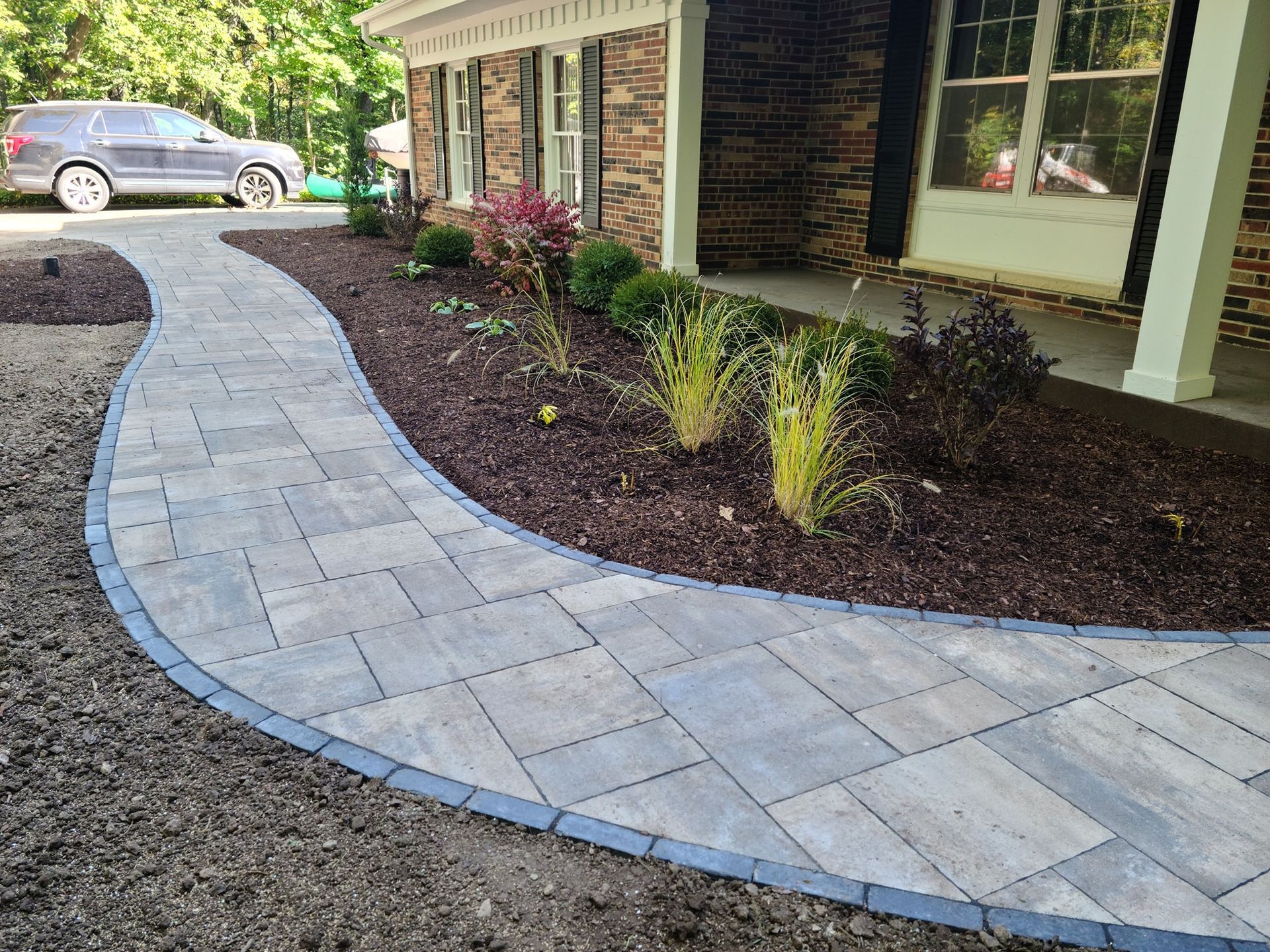 A walkway leading to a house with a car parked in front of it.