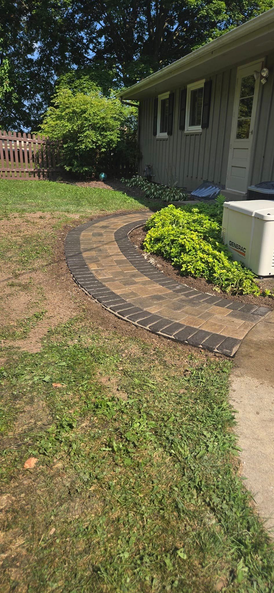 A brick walkway leading to a house with a fence in the background.