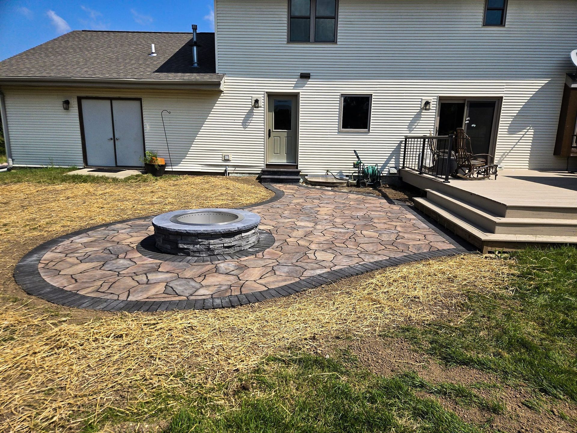 A fire pit is in the middle of a patio in front of a house.