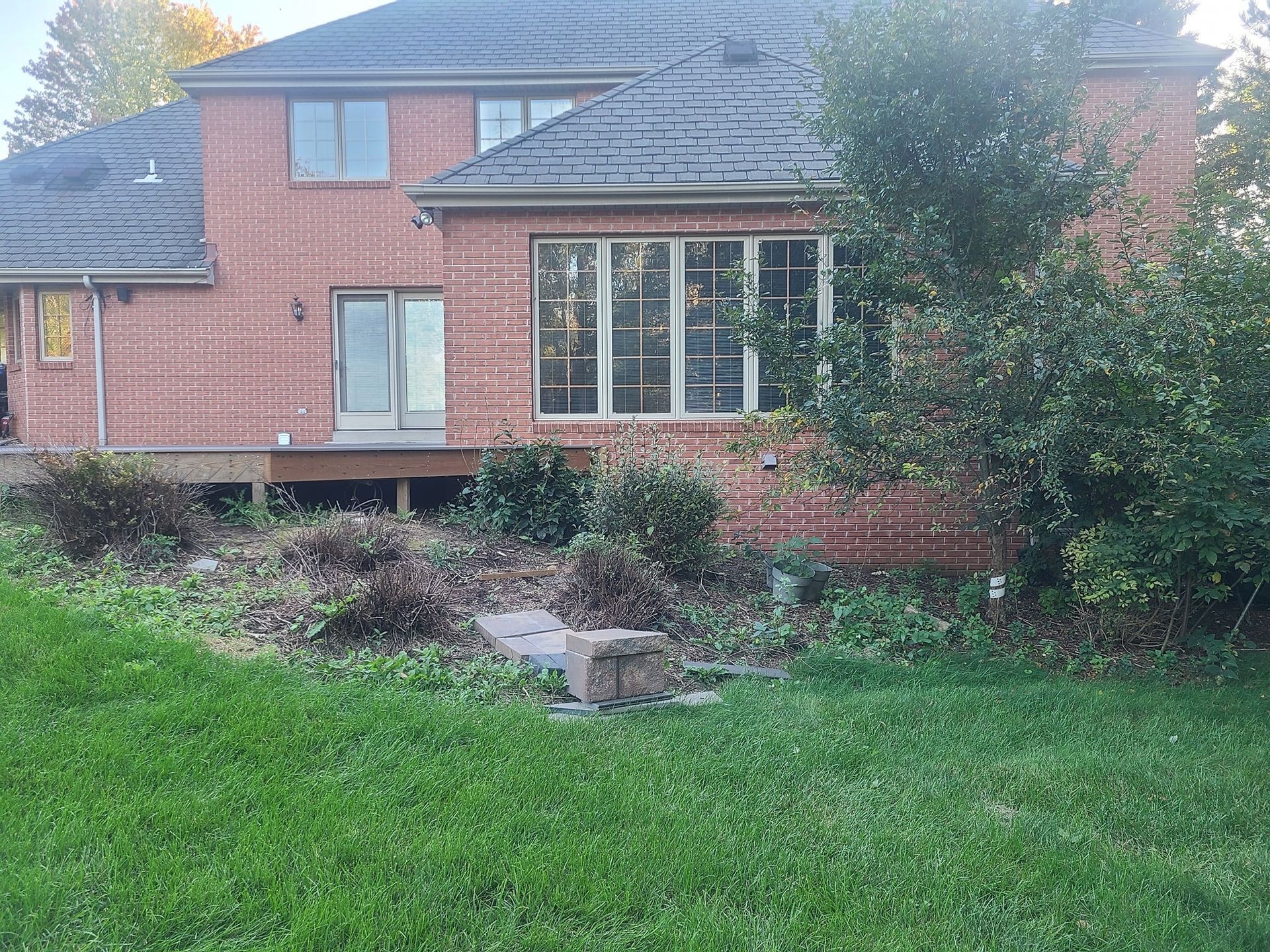 A large brick house with a slate roof is sitting in the middle of a lush green yard.