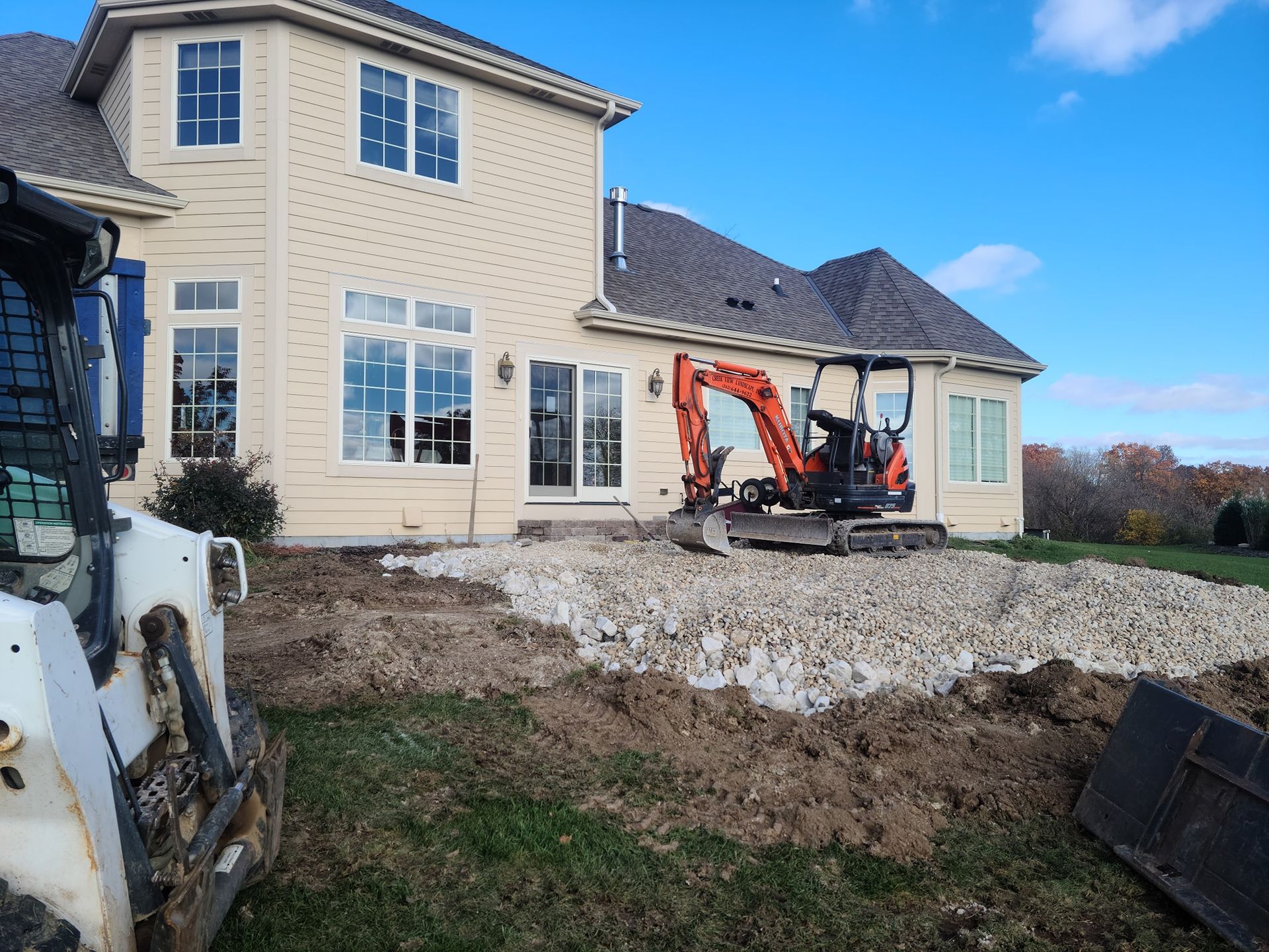 An excavator is sitting in front of a large house.