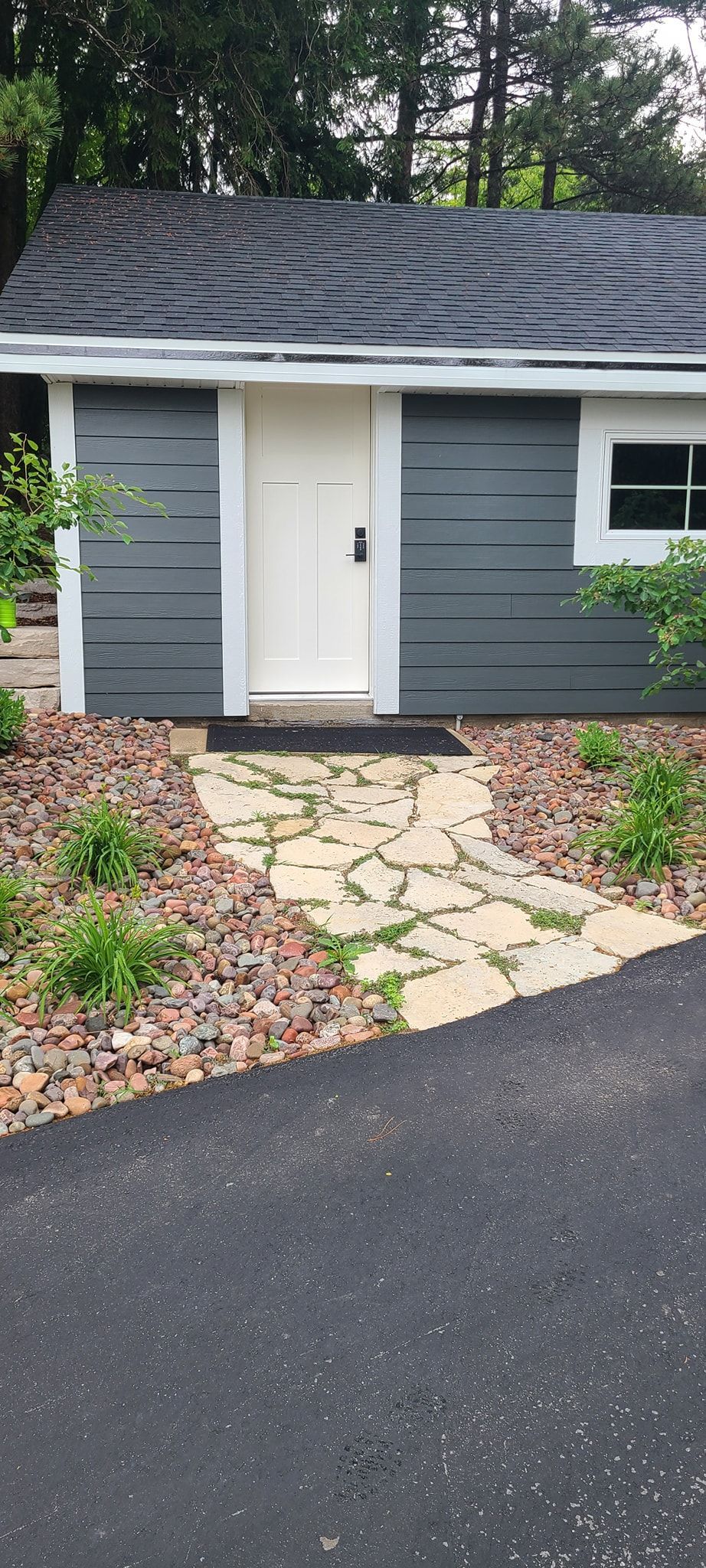 A small gray house with a white door and a stone walkway leading to it.