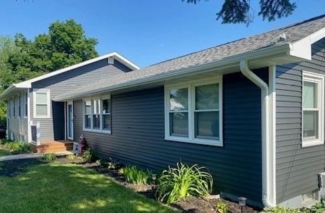 A house with a gray siding and white trim is sitting on top of a lush green lawn.