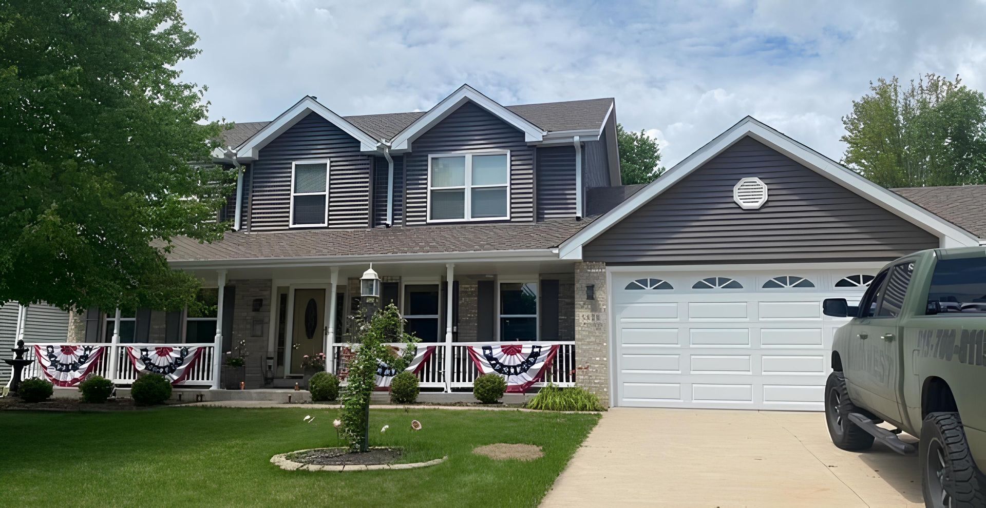 A truck is parked in front of a large house with new gray siding - After