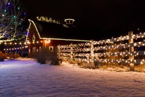Red barn and fence covered in Christmas lights on a snowy night