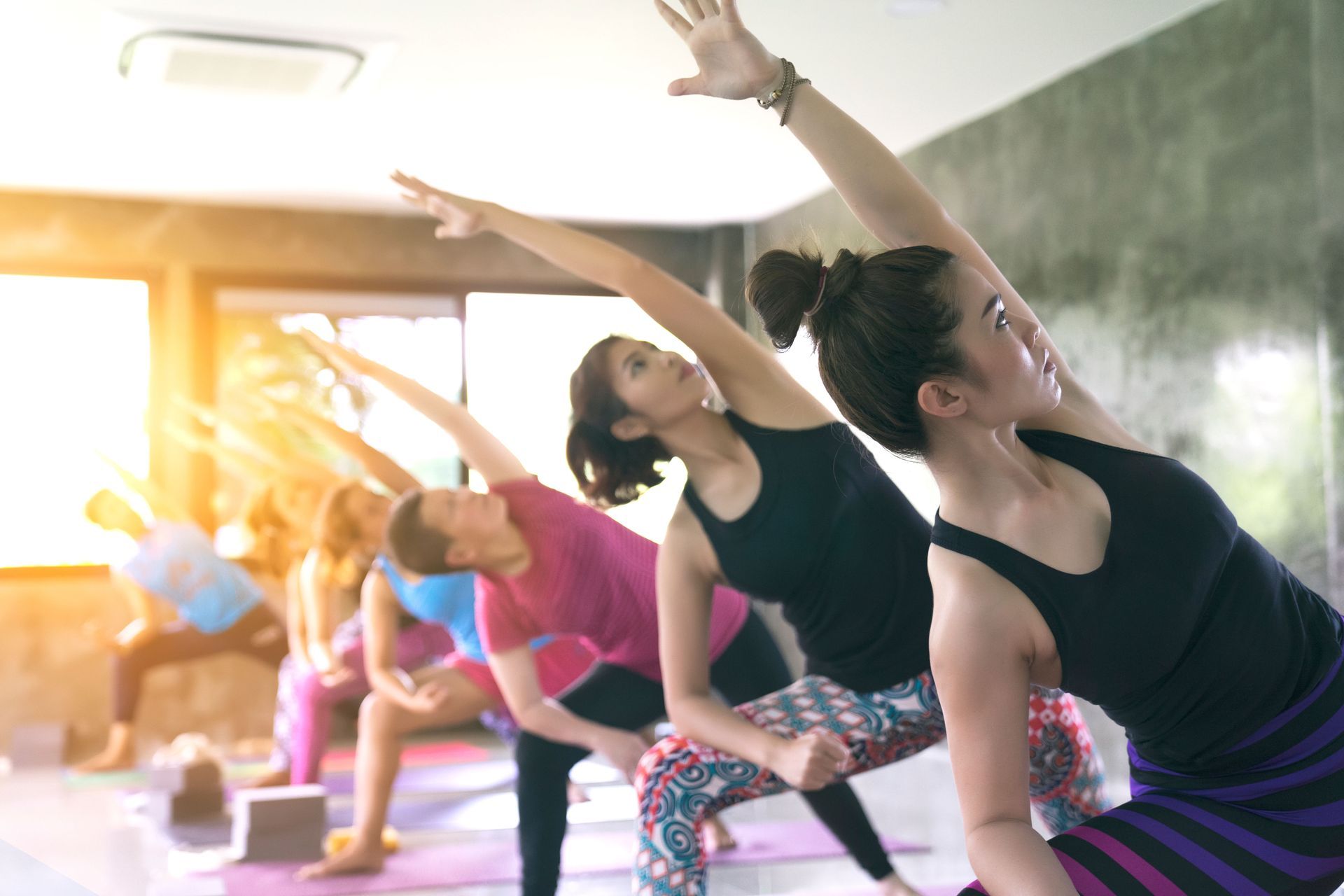 People stretching in a yoga class on mats, reaching sideways in a bright studio