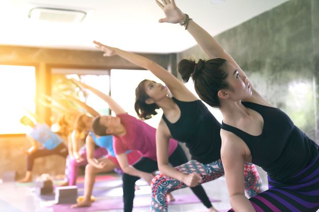 People stretching in a yoga class on mats, reaching sideways in a bright studio
