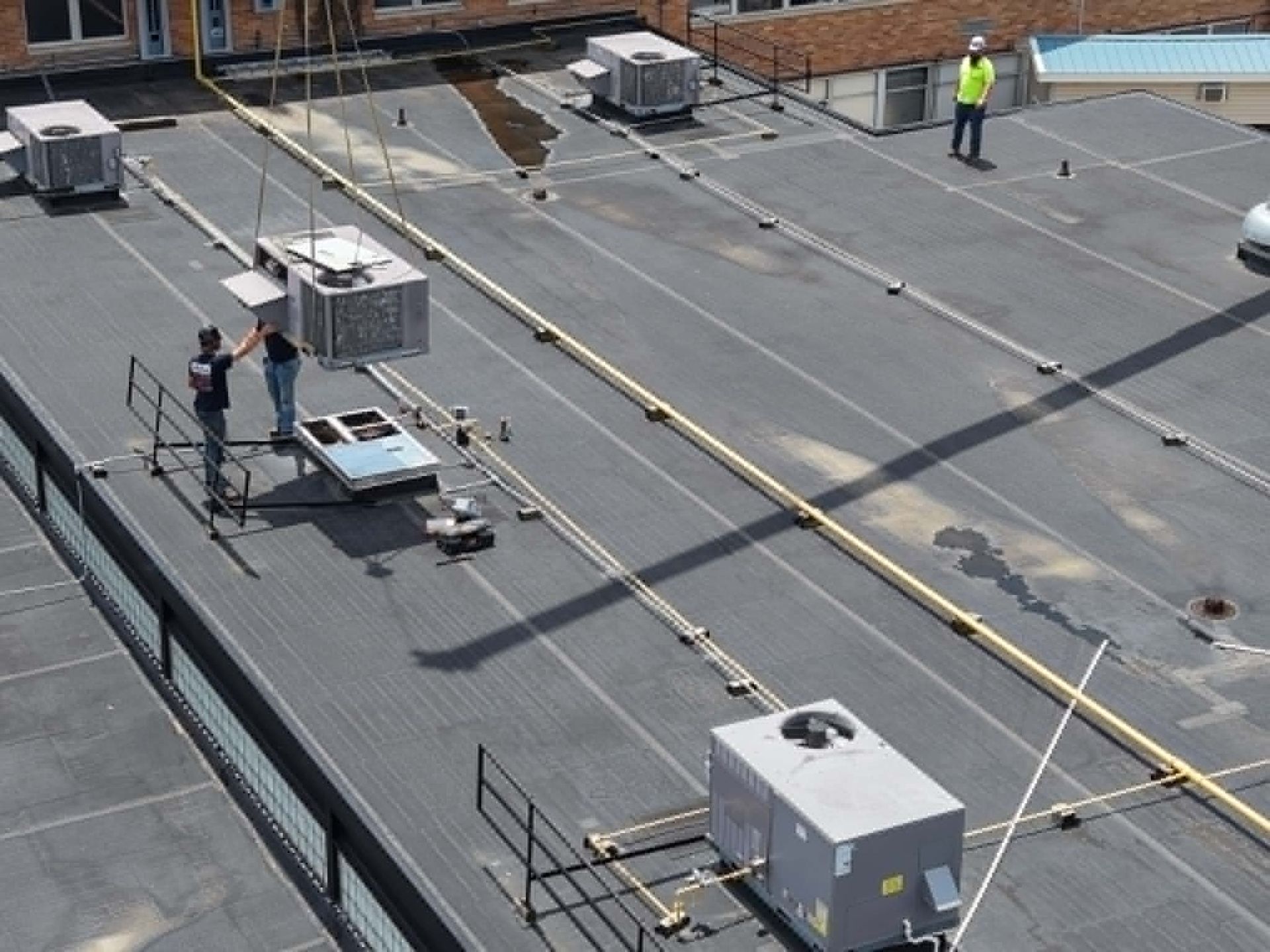 Workers and rooftop equipment on a flat industrial roof with cables and railings