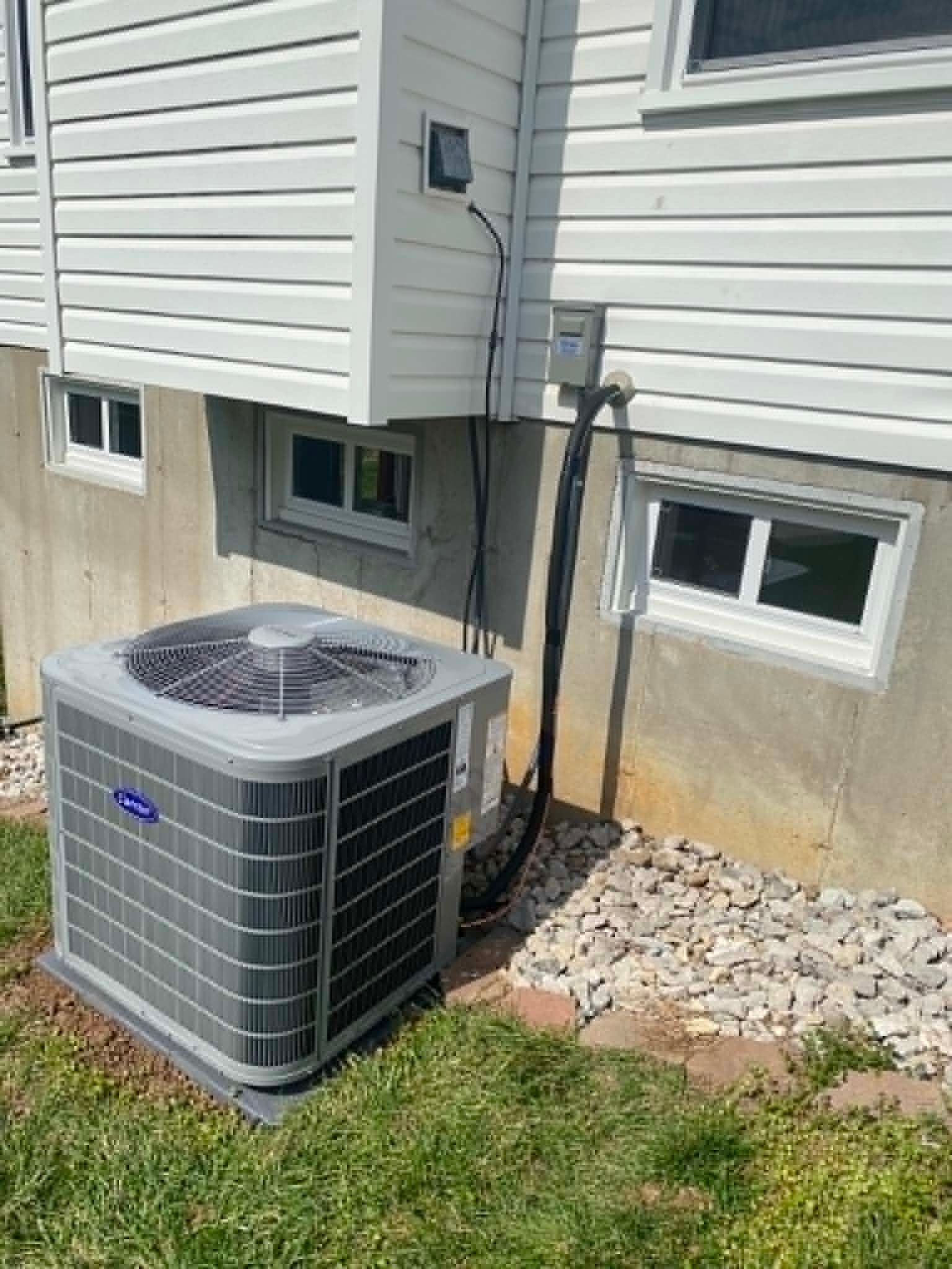 Outdoor air conditioner unit beside a house with beige siding and basement windows.