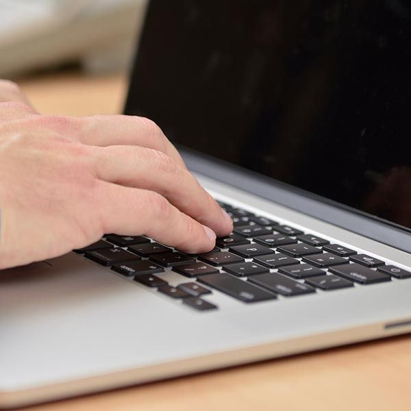 Hand typing on a laptop keyboard beside a black screen