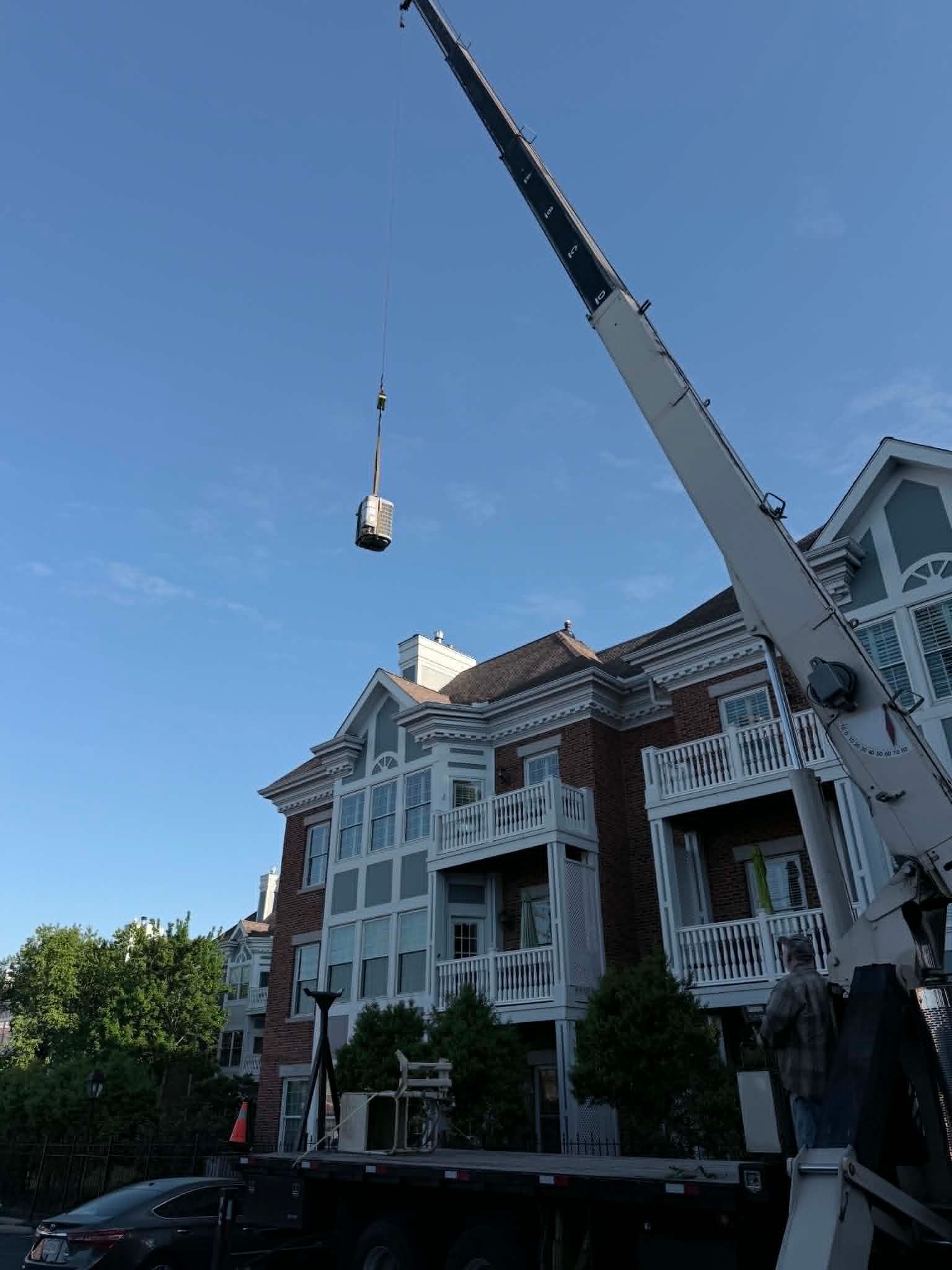 Crane lifting a bucket beside a white apartment building under a clear blue sky