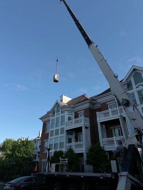 Crane lifting a bucket beside a white apartment building under a clear blue sky