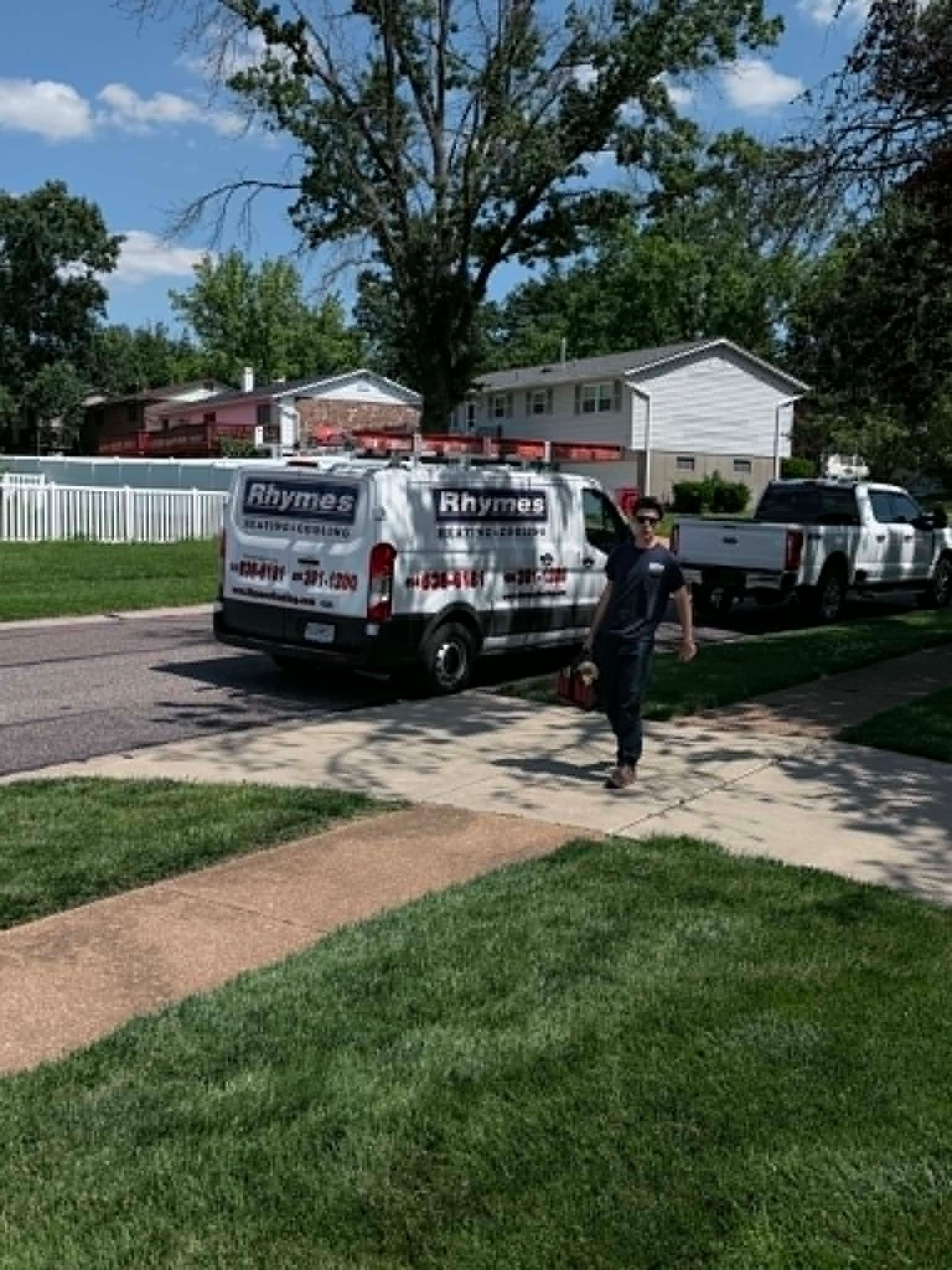 Two service vans parked on a suburban street while a worker walks on the sidewalk.