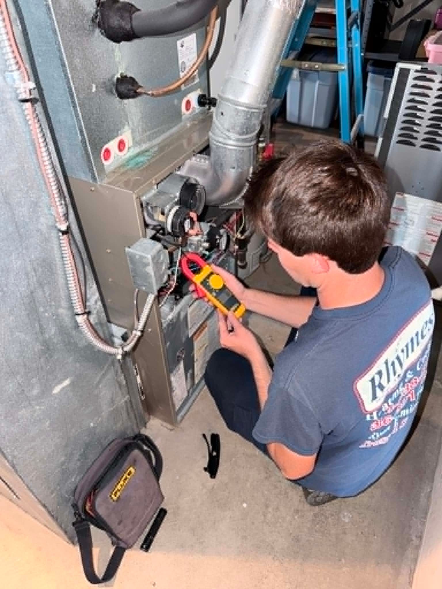 Technician using a multimeter to inspect furnace wiring in a utility room