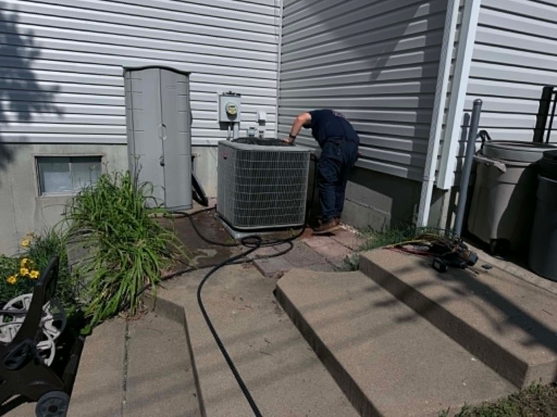 Technician servicing an air conditioner unit beside a house deck.