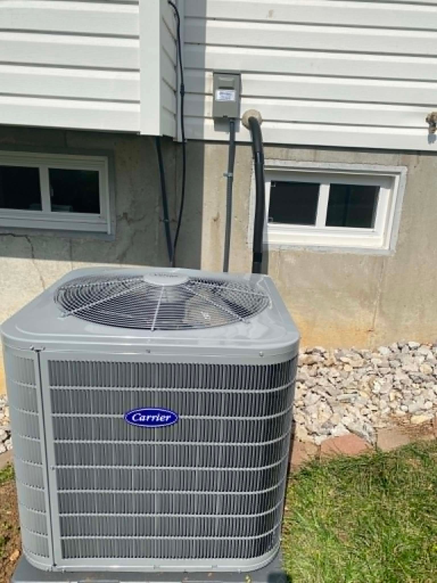 Carrier air conditioner unit beside a house wall with small windows and gravel landscaping