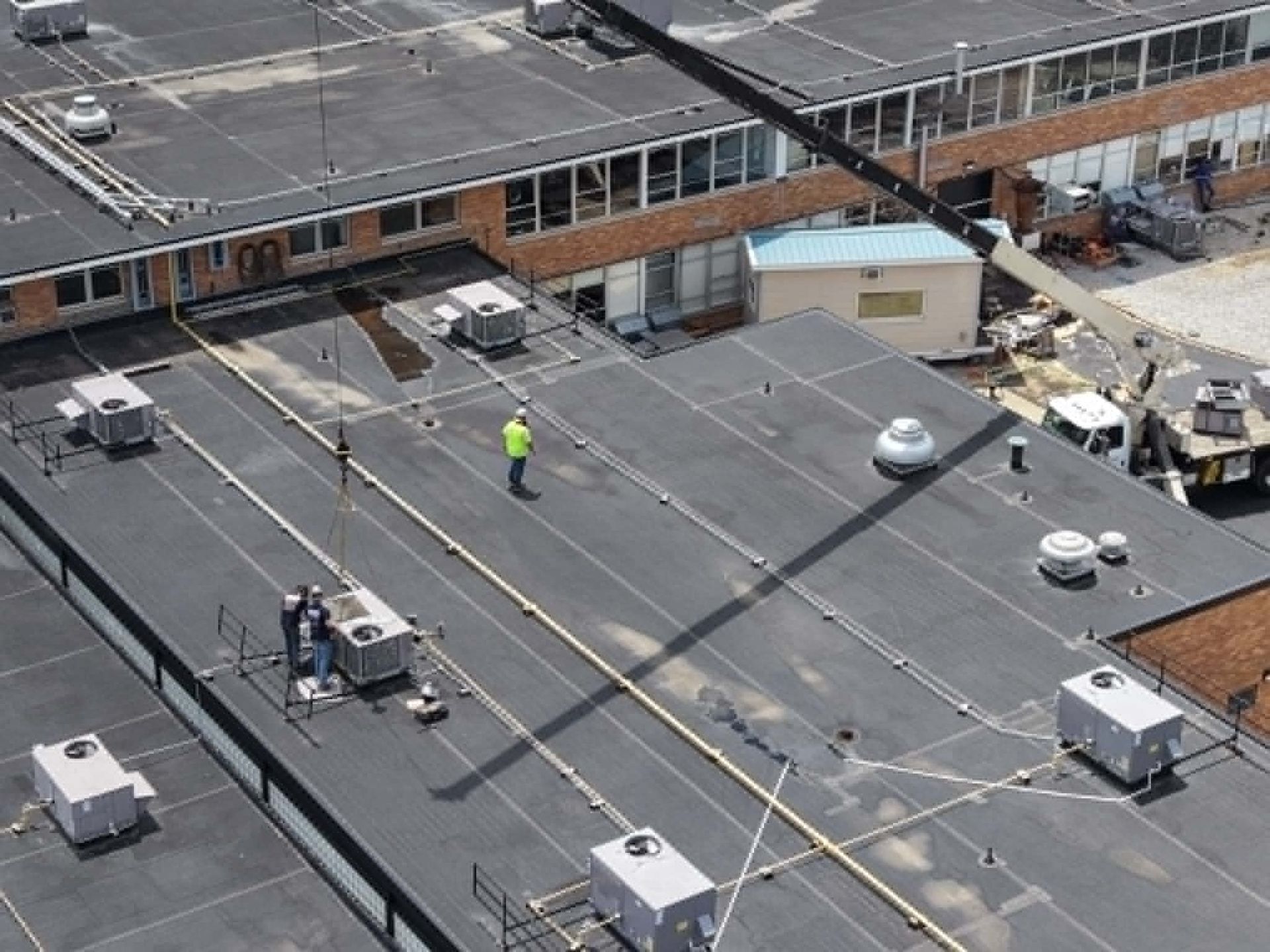 Rooftop with HVAC units and workers inspecting a large flat commercial roof