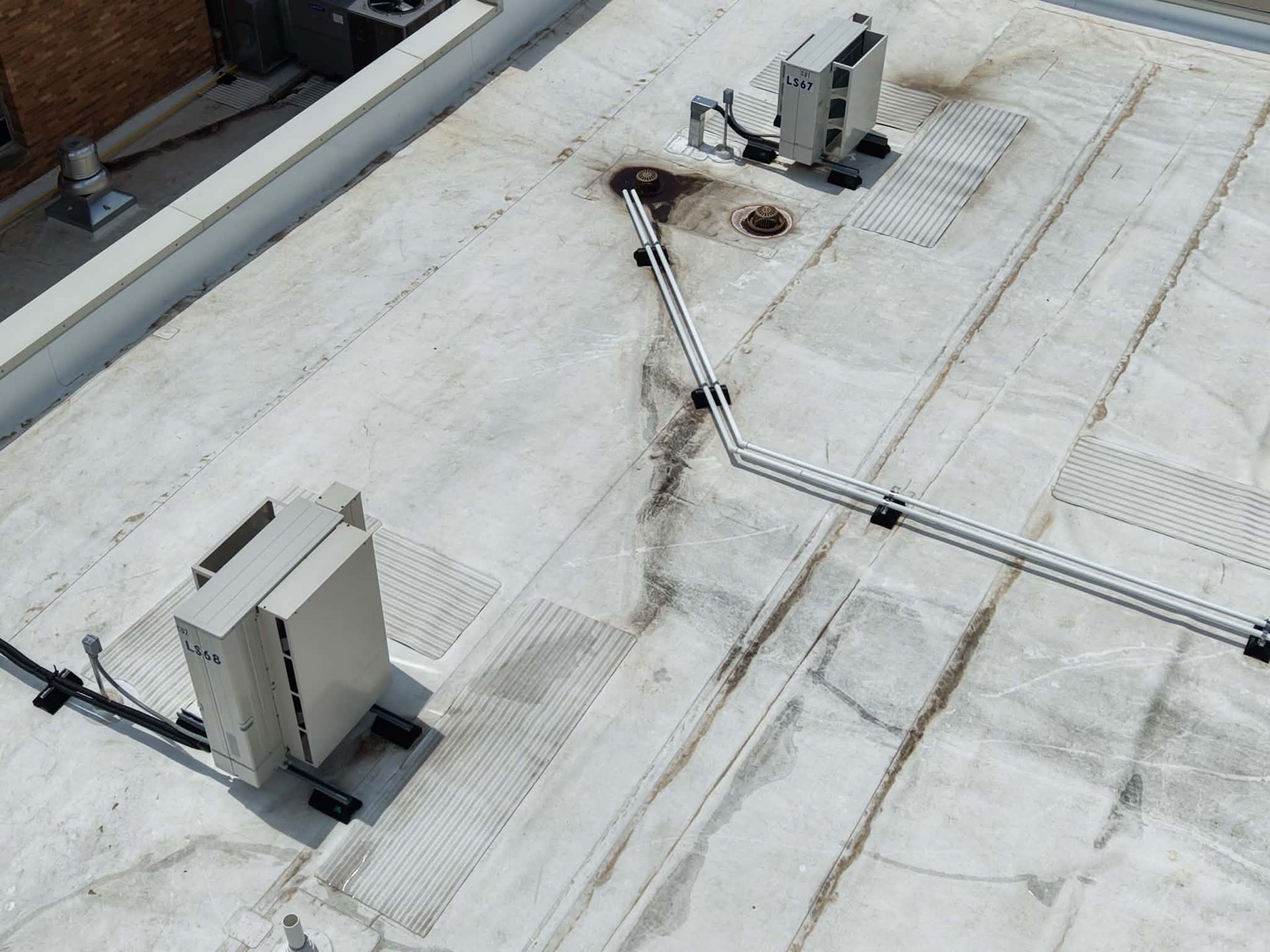 Rooftop HVAC units connected by white conduit lines on a flat, weathered roof.