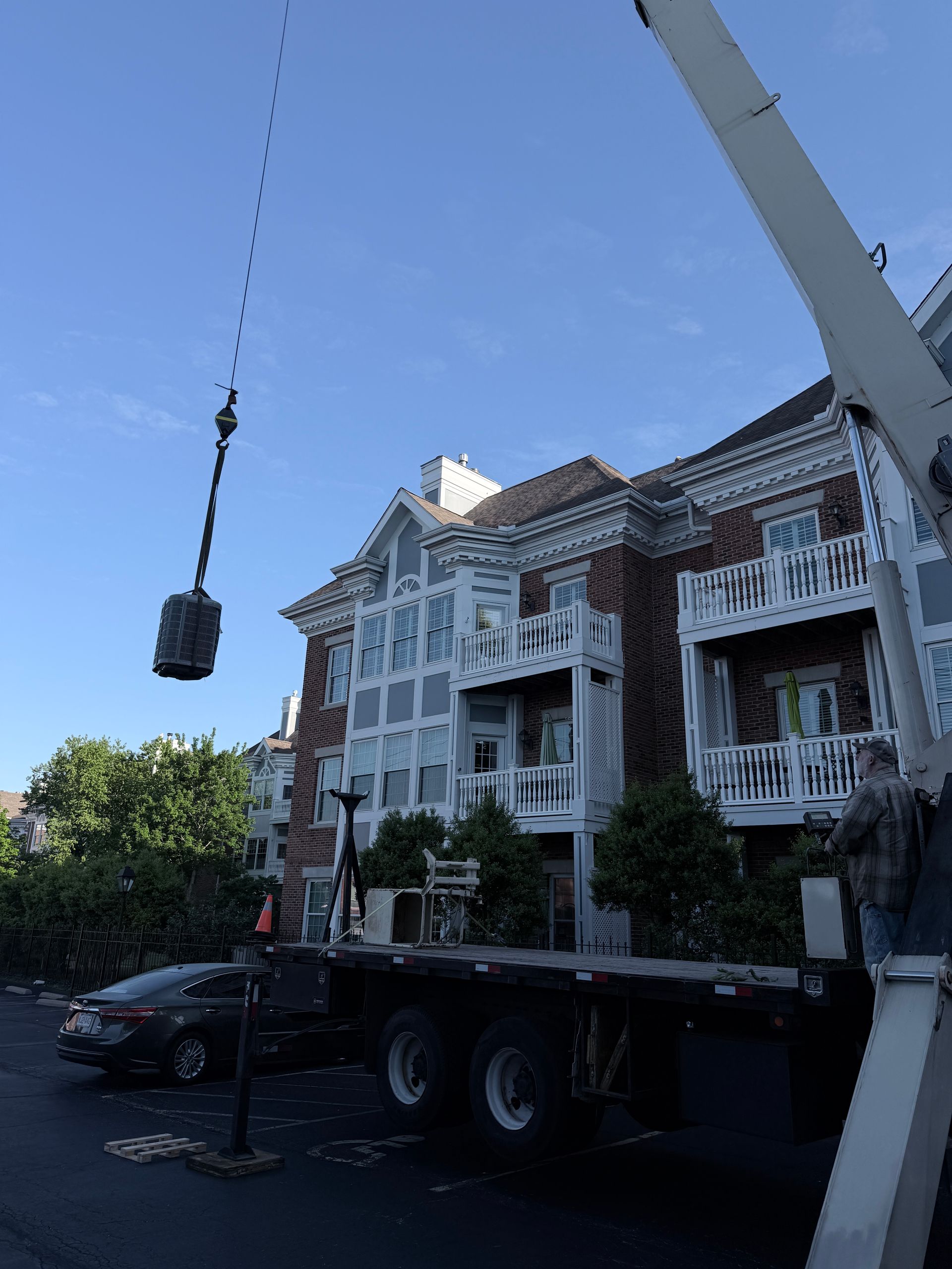 Crane lifting a hanging load beside a white Victorian-style building and parked truck